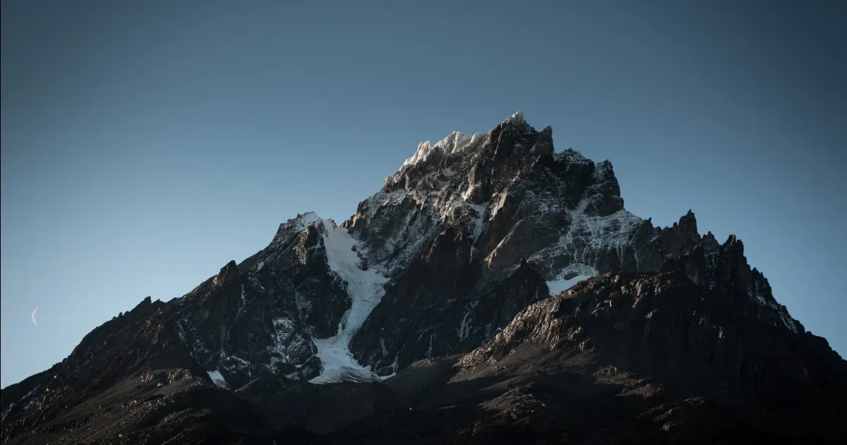 The Cerro Paine Grande in Chile, slightly covered in snow, photographed in the morning with the crescent moon on its side.